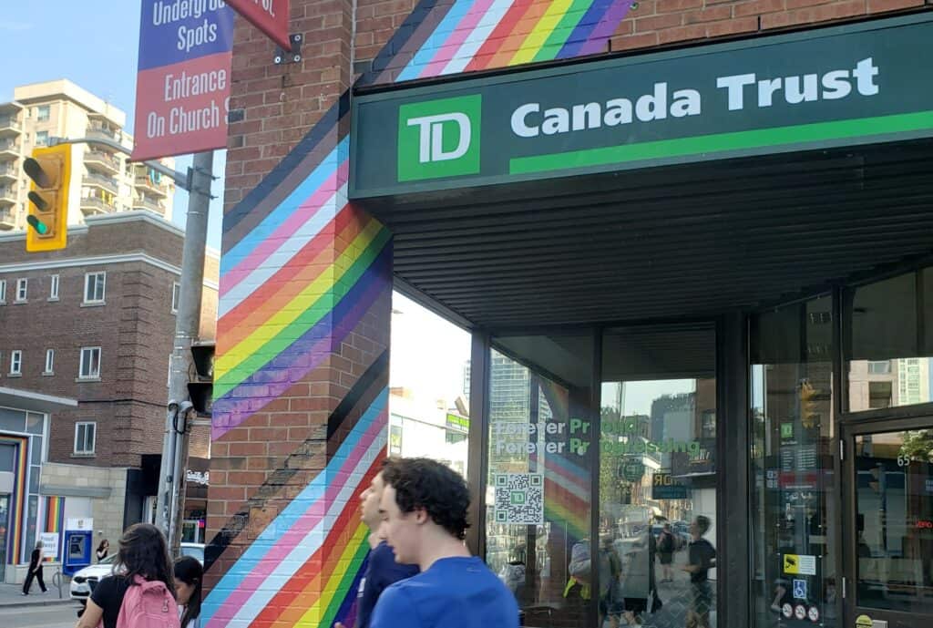 Photo of the front of a TD bank store in the gay village in Toronto, with rainbow stripes on it.