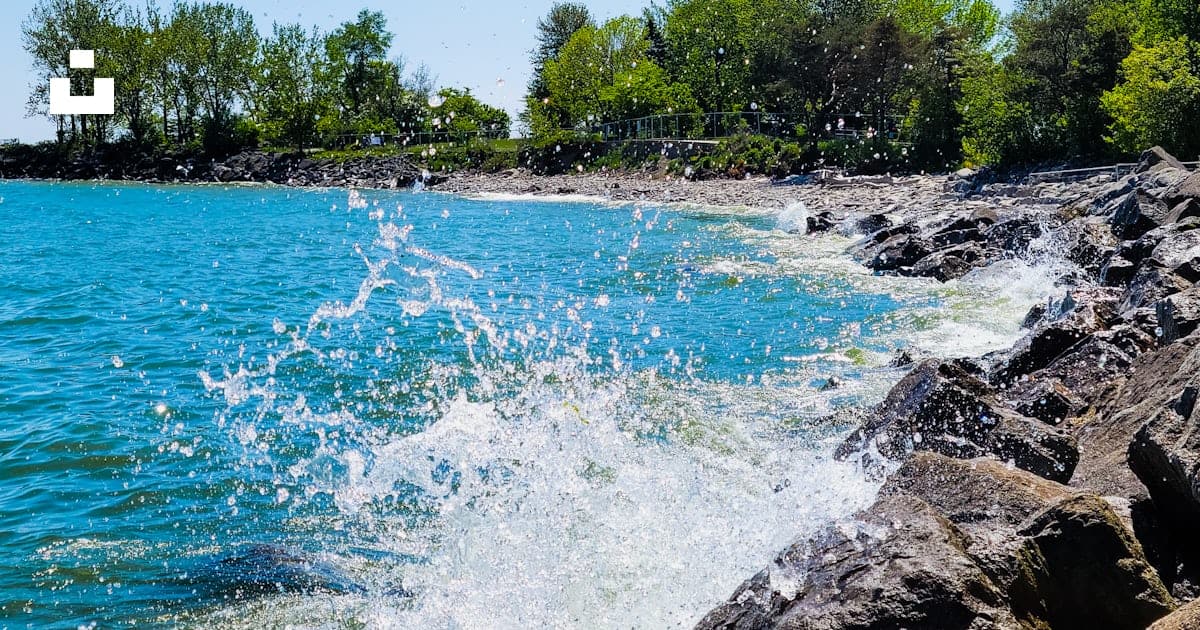 Photo of a rocky beach with wave splashing water in the foreground on a summer day.